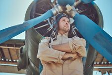 Valiant Handsome Pilot In A Full Flight Gear Standing With Crossed Arms Near Military Airplane. Royalty Free Stock Photos