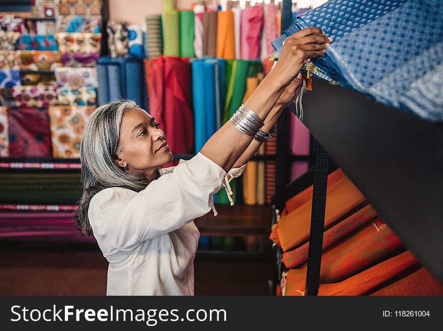 Mature woman looking through cloth rolls in a fabric shop