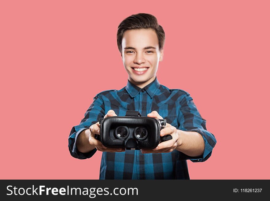 Young man with vr headset looking at camera with toothy smile and sharing. studio shot, isolated on pink background. Young man with vr headset looking at camera with toothy smile and sharing. studio shot, isolated on pink background.