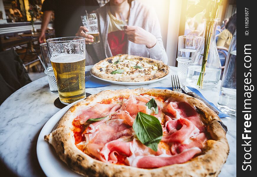 Woman drinking beer and eating delicious pizza Salsiccia e Carciofi made from Artichoke heart, Campania buffalo mozzarella, black pork sausage, pecan and San Marzano DOP tomato, Campania buffalo mozzarella sunlight flare. Woman drinking beer and eating delicious pizza Salsiccia e Carciofi made from Artichoke heart, Campania buffalo mozzarella, black pork sausage, pecan and San Marzano DOP tomato, Campania buffalo mozzarella sunlight flare