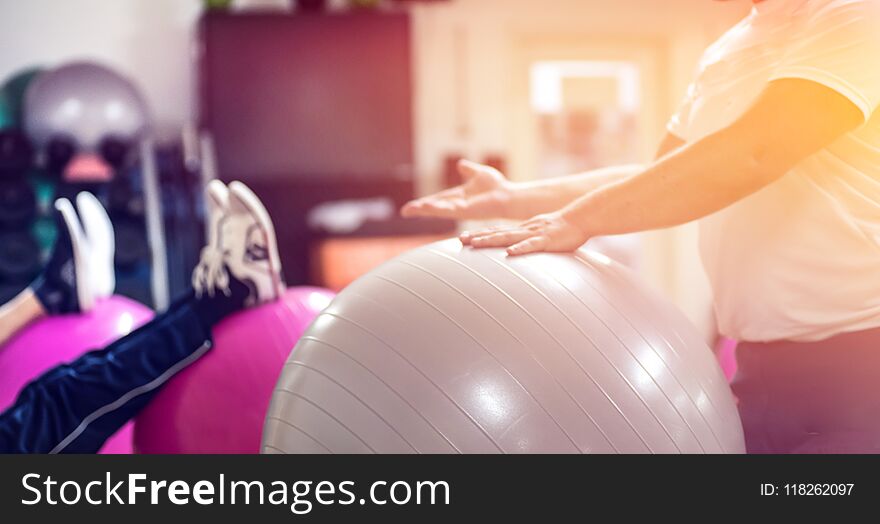 Exercising with personal trainer on large stability ball in studio fitness back physiotherapy