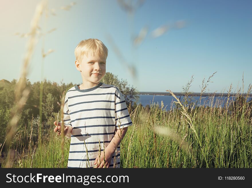 Little blond boy smiling and looking at camera on nature. Summer activity. Field with high grass. Little blond boy smiling and looking at camera on nature. Summer activity. Field with high grass.