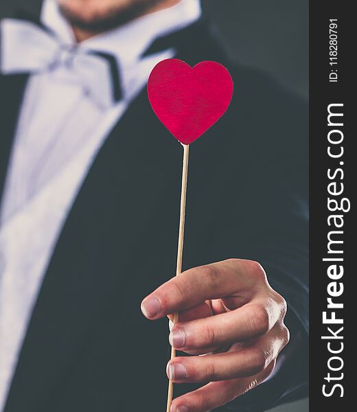 Valentines day. Love concept. Holidays and celebration. Elegant young guy wearing suit white shirt bow tie holding heart stick in hand. Valentines day. Love concept. Holidays and celebration. Elegant young guy wearing suit white shirt bow tie holding heart stick in hand