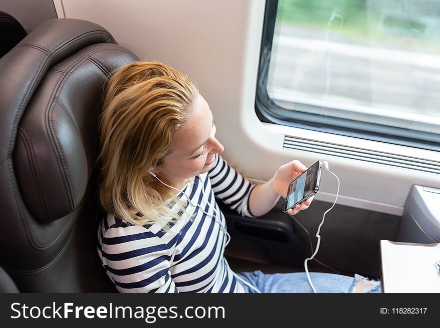 Woman communicating on cellphone using headphone set while traveling by train in business class seat. Woman communicating on cellphone using headphone set while traveling by train in business class seat.