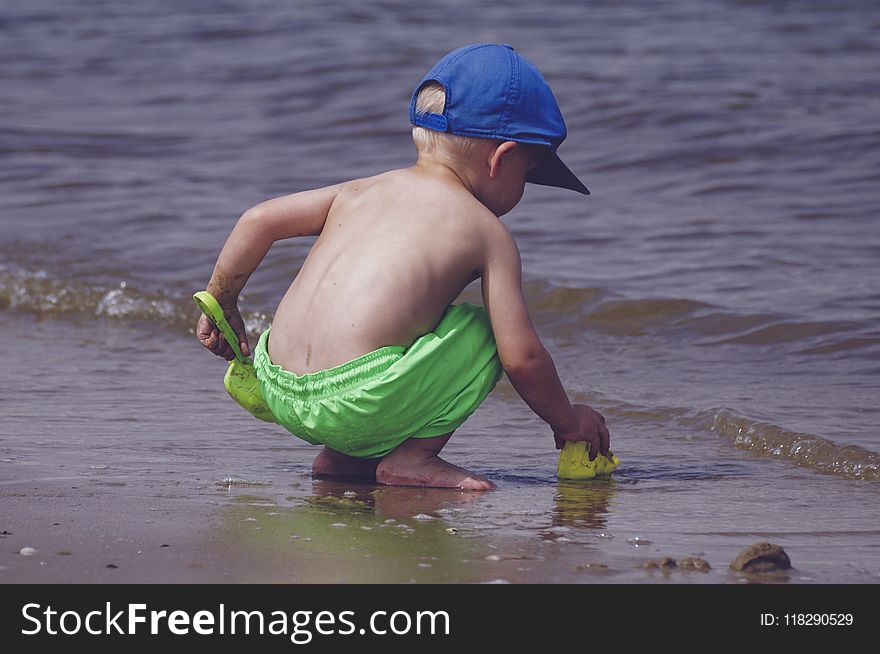Boy In Blue Cap And Green Shorts Playing On Seashore