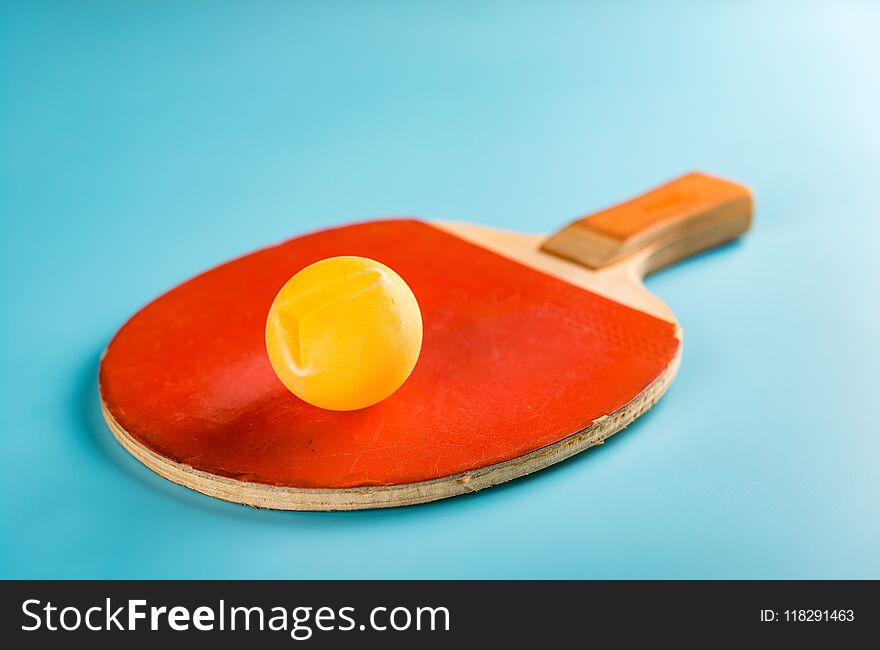 Old pingpong racket and a dented ball on a blue background