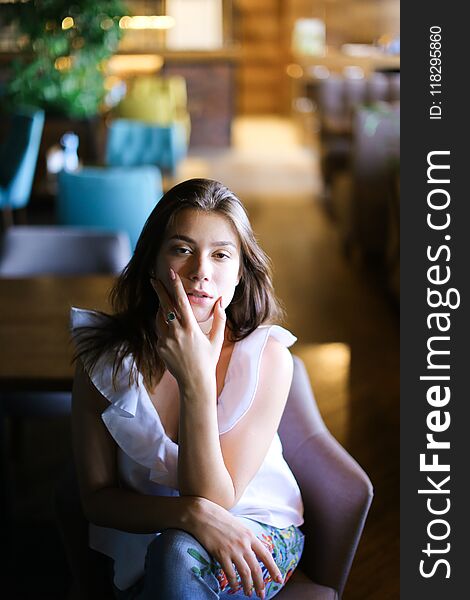 Stylish Photo Model Sitting At Cafe And Wearing White Blouse With Ethnic Jeans.