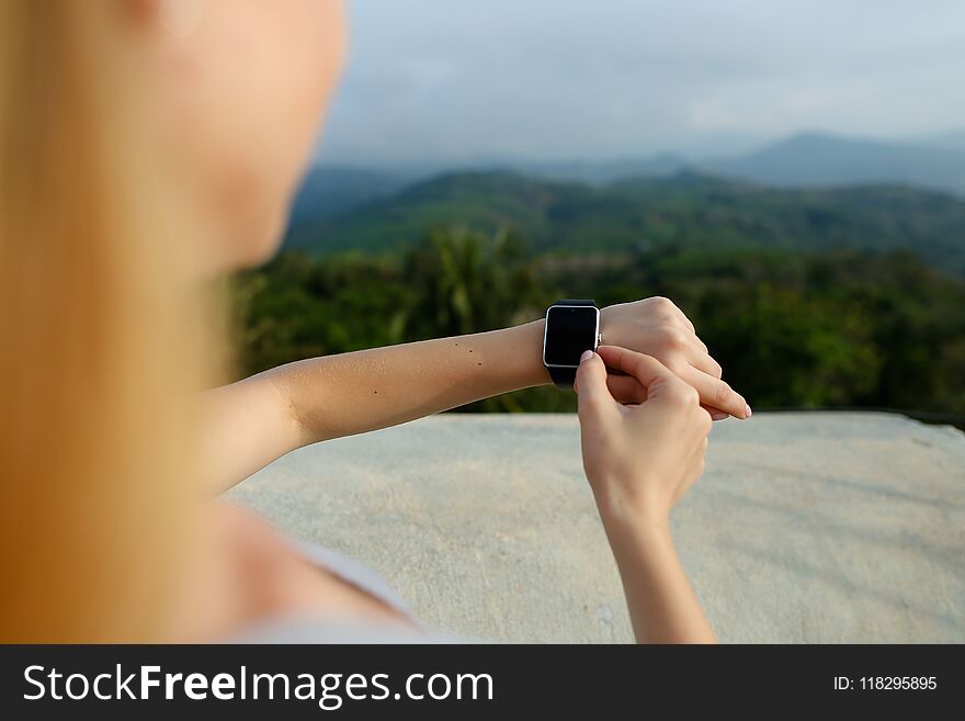 Female hands using smart watch, mountains in background. Concept of modern technology and nature.