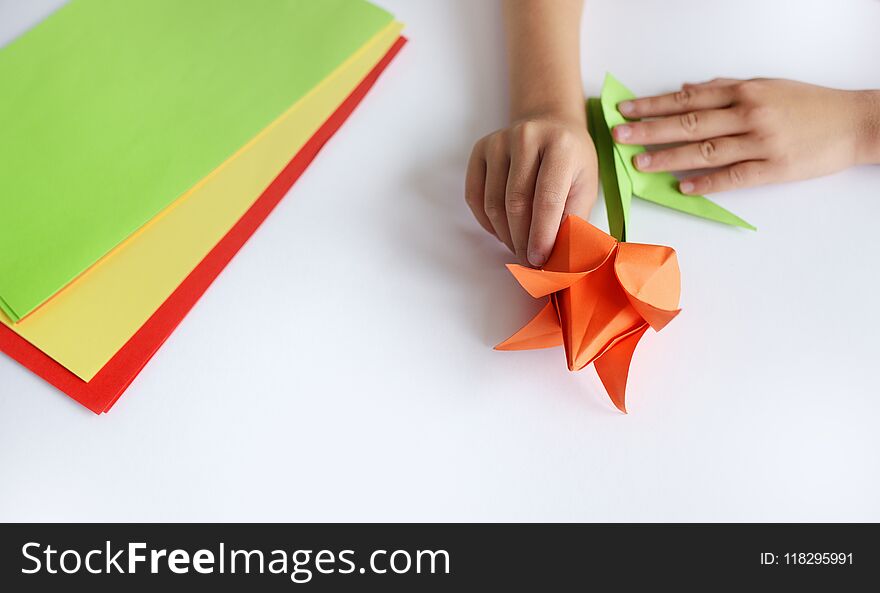 Children`s hands do origami from colored paper on white background. lesson of origami
