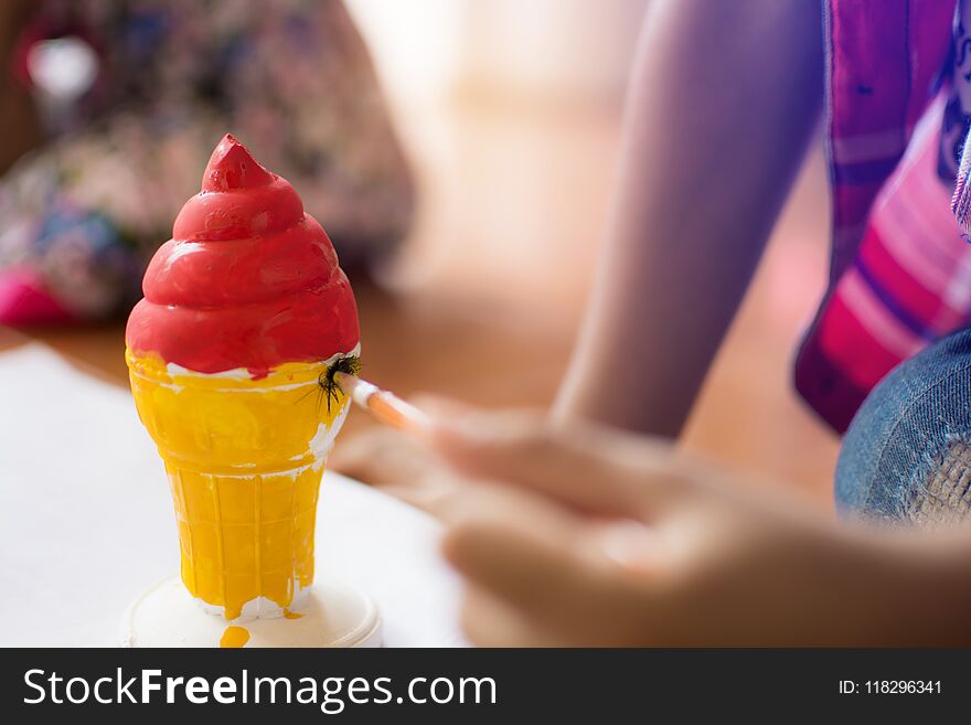 Close up hand of little boy painting plaster ice cream cone with red and yellow