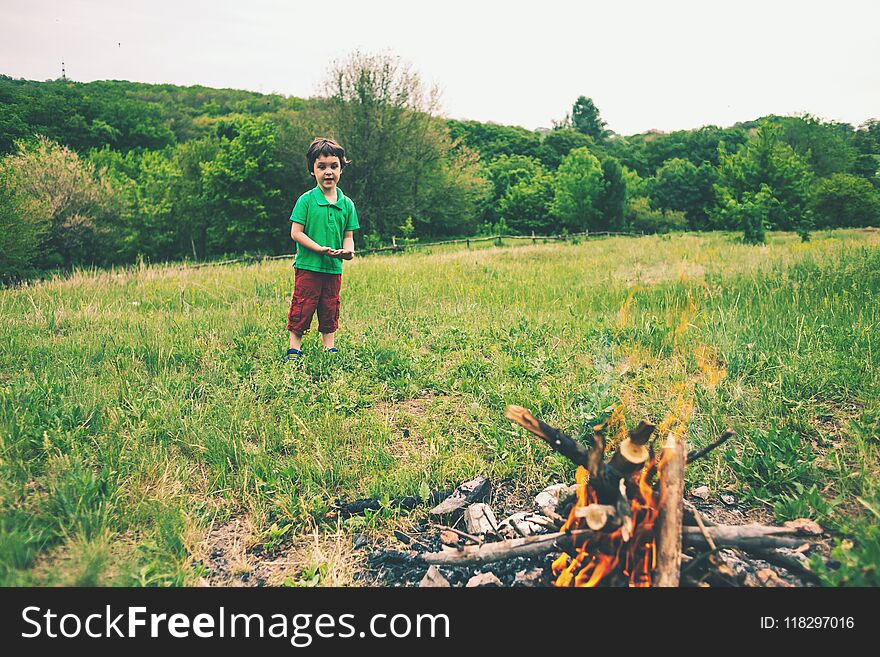 The boy is standing by the fire. The child collects firewood for the bonfire. Camping in nature. Picnic in the forest glade.