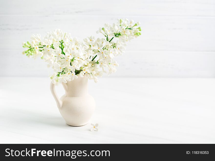 Blooming white lilac in ceramic vase jar on white table background with copy space. Blooming white lilac in ceramic vase jar on white table background with copy space