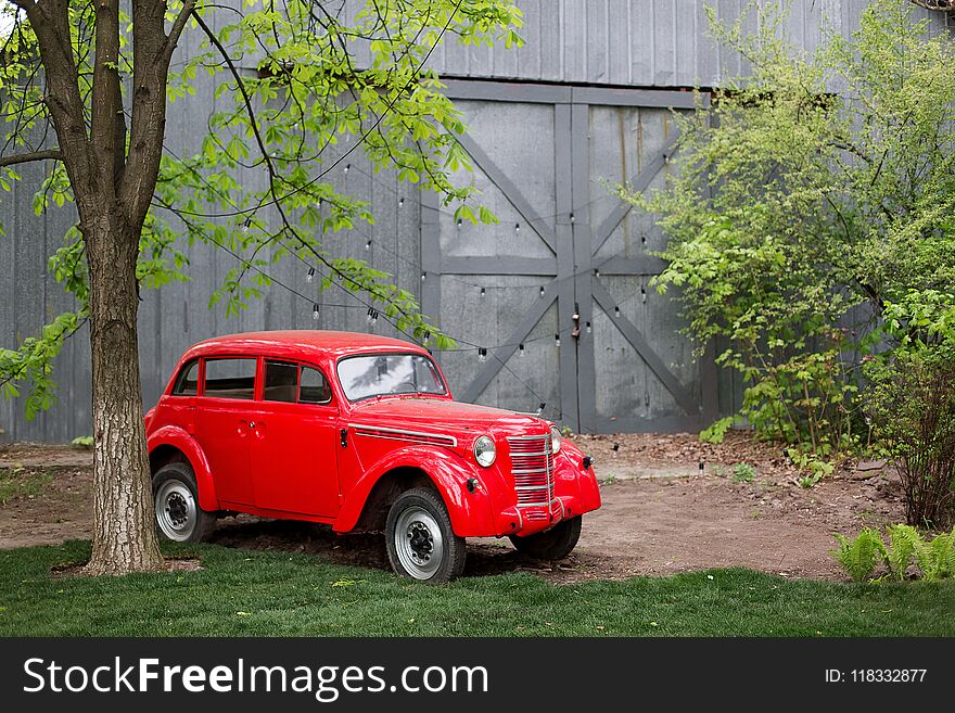 Red retro small vintage car standing in the garden in the summer. Location