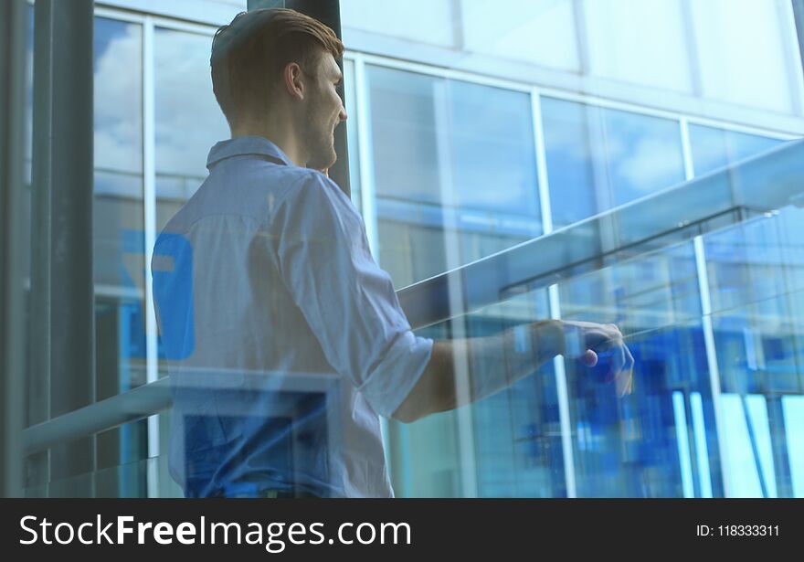 Young man standing near window in his office while thinking about his goals.