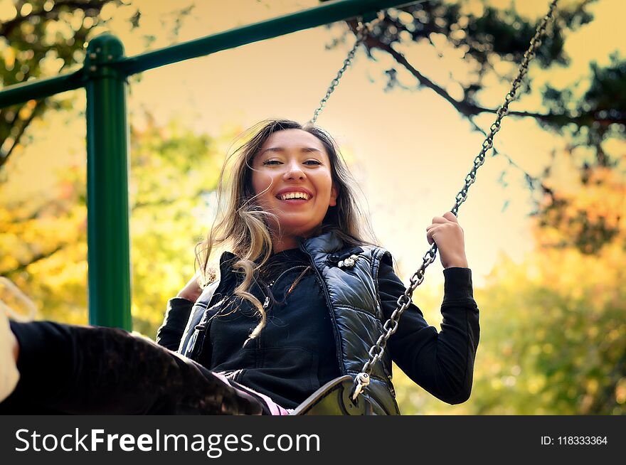 The girl of the eastern appearance laughs and swings on a swing. Selective focus