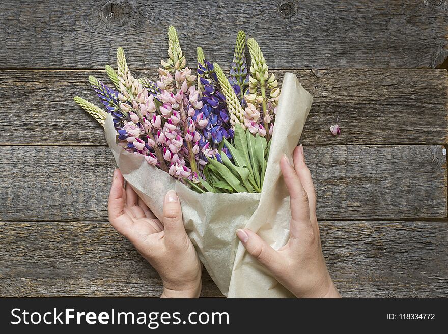 Women`s hands are collected in a bouquet of lupine flowers on a wooden background