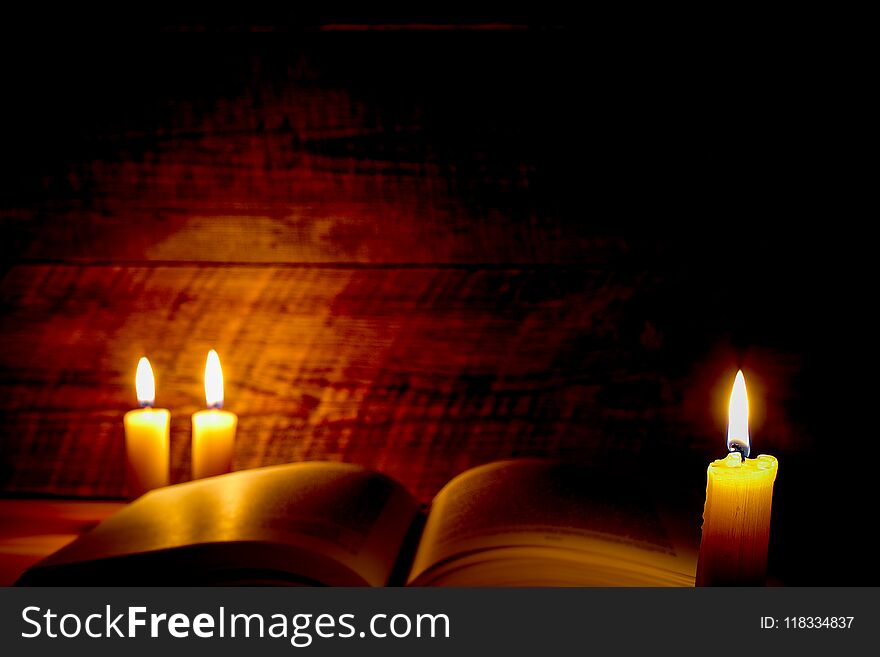 Old book on a wooden table by candlelight at night