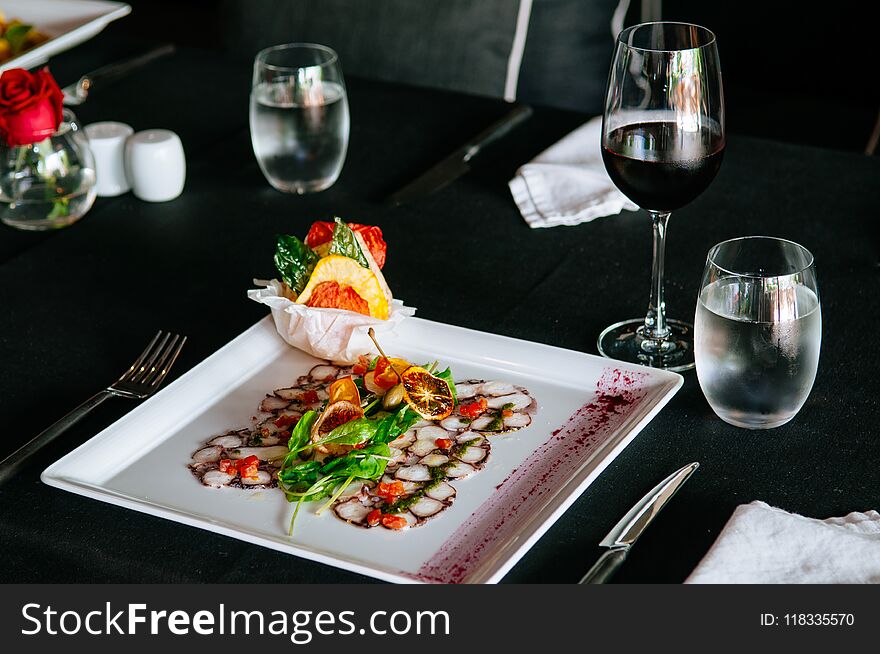 Fresh octopus carpacio with citrus spinach salad pesto balsamic dressing, fine dinning table setting