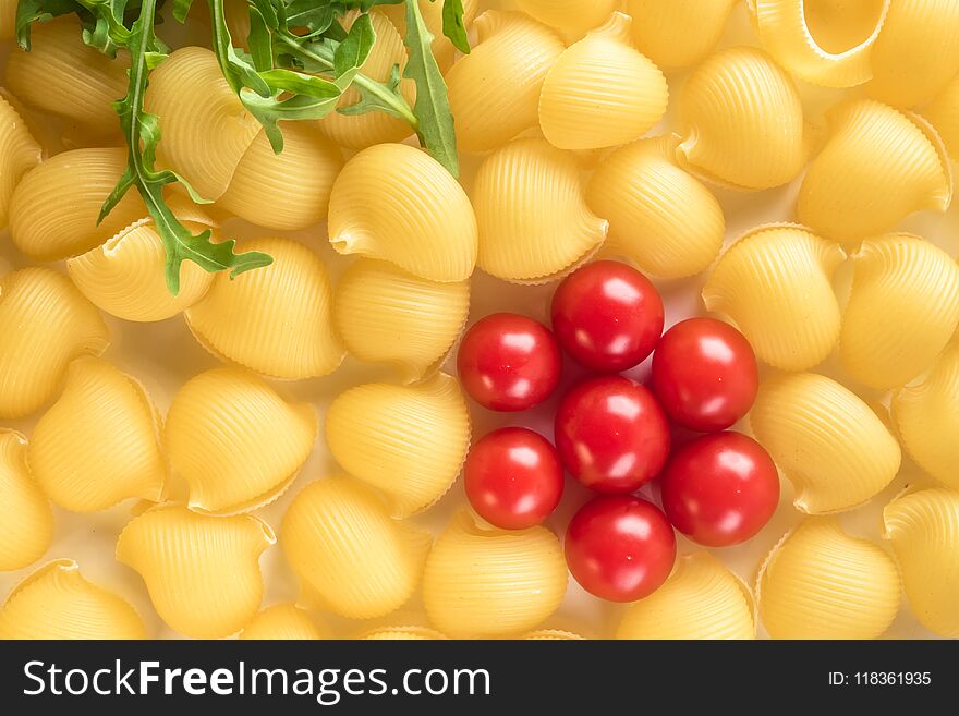 Food background Uncooked Macaroni Lumaconi close-up macro red Cherry Tomatoes in flower form and leaves Rucola Salad Concept set of ingredients for Pasta