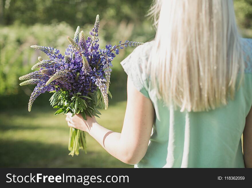 The girl is standing with her back in the field with a bouquet of lupines. The girl is standing with her back in the field with a bouquet of lupines