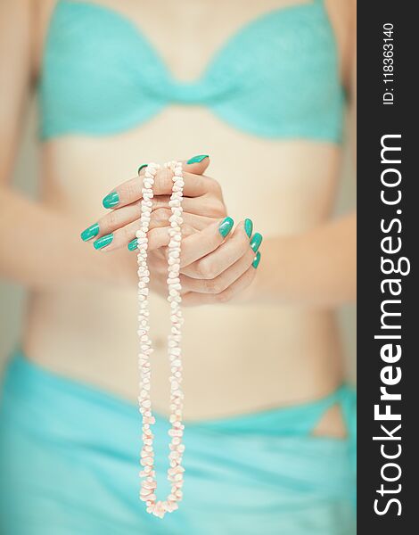 Beautiful woman hands with perfect blue nail polish holding coral necklace, happy bikini beach mood
