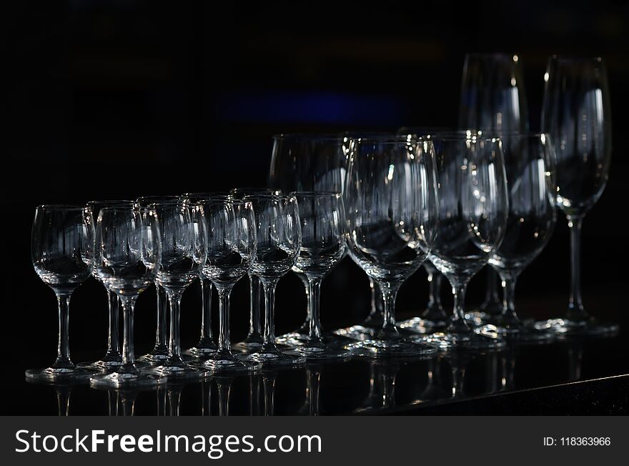 Rows of the empty wineglasses and empty glasses for vodka, going to unsharpness, stands on a black surface bar counter. Rows of the empty wineglasses and empty glasses for vodka, going to unsharpness, stands on a black surface bar counter.