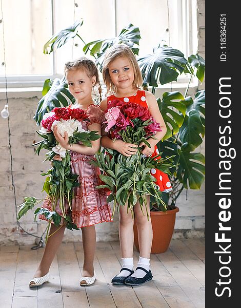 Two cute little girls with peonies. Two beautiful friends having fun, hugging and smiling