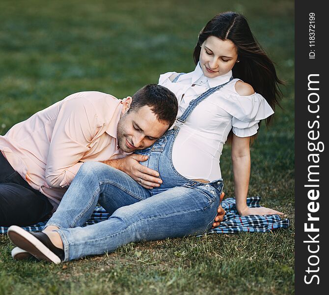 Father-to-be listening to baby moving inside belly. Pregnant couple hugging in nature. Happiness, love, family concept. Father-to-be listening to baby moving inside belly. Pregnant couple hugging in nature. Happiness, love, family concept