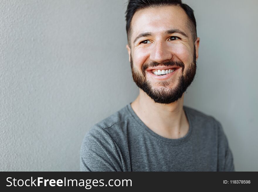 Portrait of a beautiful stylish guy dressed in a grey blank t-shirt standing on a brick grey wall background. Empty space for log