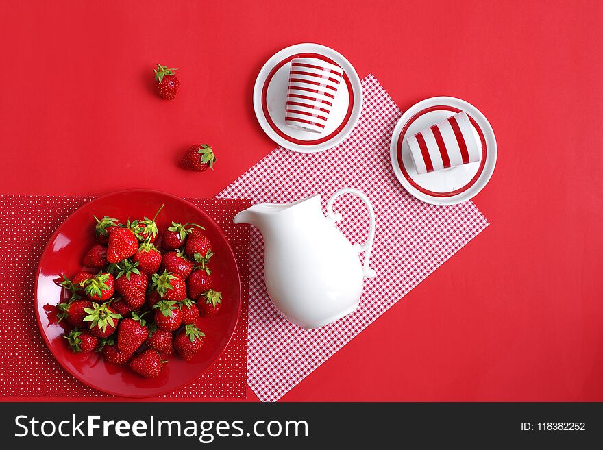 Bright red ripe summer strawberries and a white jug with cream on a red background. Top view.