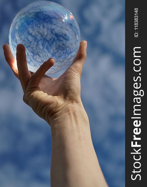 Contact juggling. Hand and acrylic ball against the sky. Cumulus clouds are reflected in the sphere. Close-up