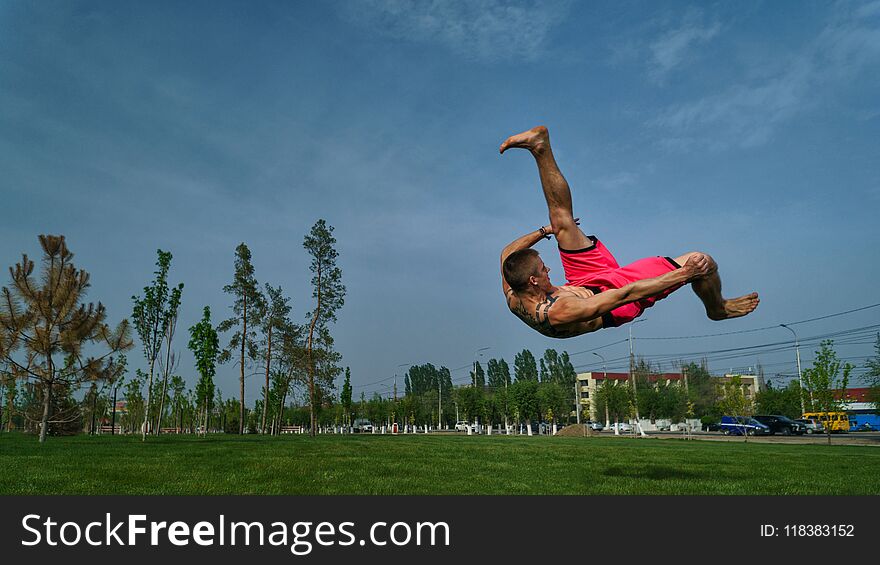 Tricking on lawn in park. Man does somersault ahead. Martial arts and parkour. Street workout.