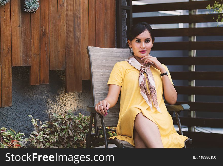 Woman Wearing Yellow Short-sleeved dress Sitting on Black Metal Armchair