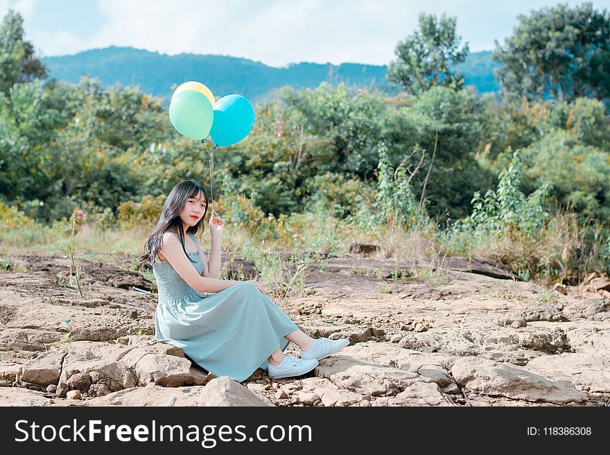 Woman Sitting On Rocks Holding Balloons