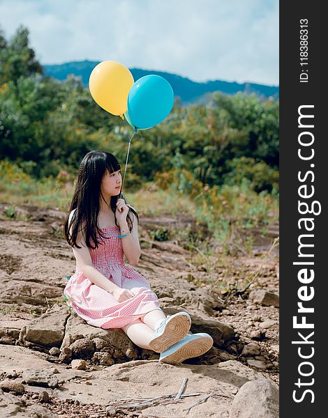 Woman Wearing Pink Dress Sitting on Ground Holding Two Balloons