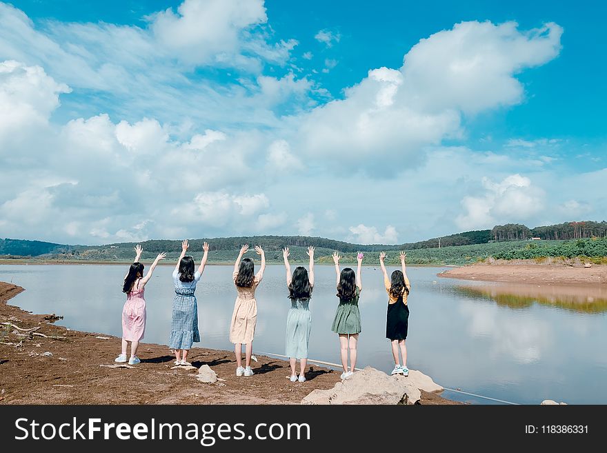 Six Girls Raise Their Hands in Front of Body of Water