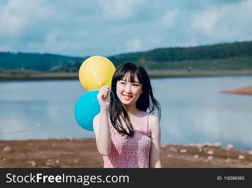 Woman in Pink Thick Strap Top Holding a Yellow and Blue Balloons