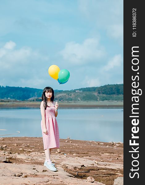 Woman Holding Balloons Standing on Beige Sand