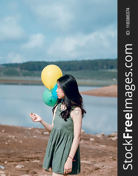 Woman in Green Crew-neck Sleeveless Mini Dress Holding Balloons Near Body of Water