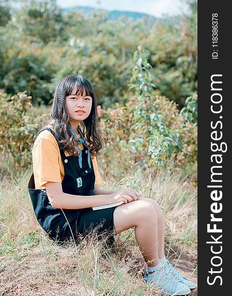 Girl in Black Dungaree and Orange Shirt Sitting of Grass Field