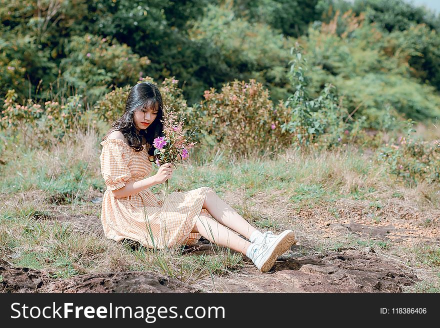 Woman Sitting on Ground and Holding Flower