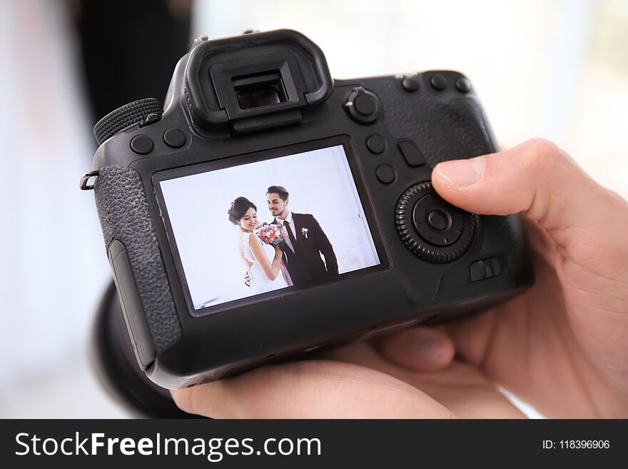 Professional Photographer Holding Camera With Lovely Wedding Couple On Display