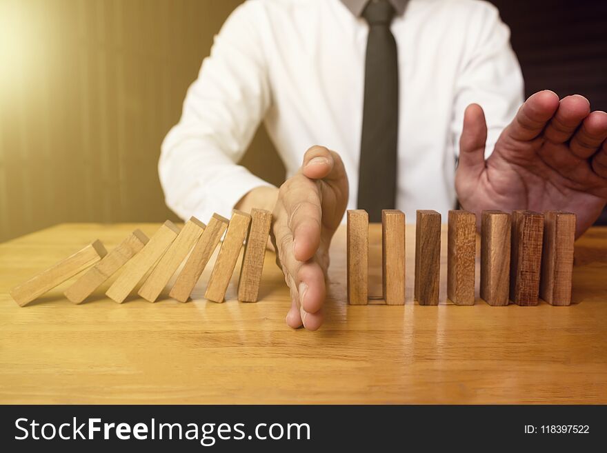 Hand of businessman is stoping falling wooden domino effect from
