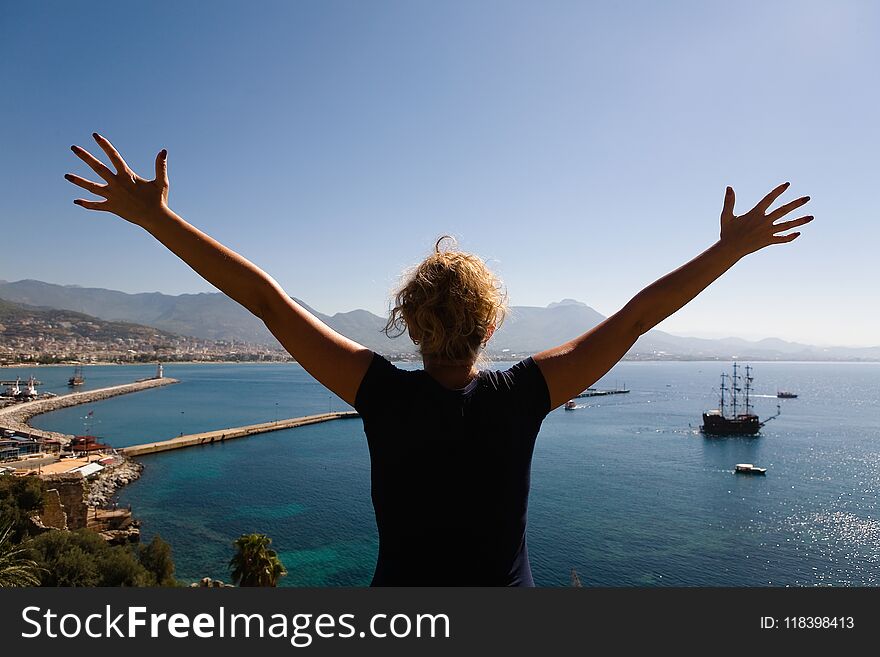 A slender girl spread her arms in different directions against the backdrop of Alanya. Turkey.