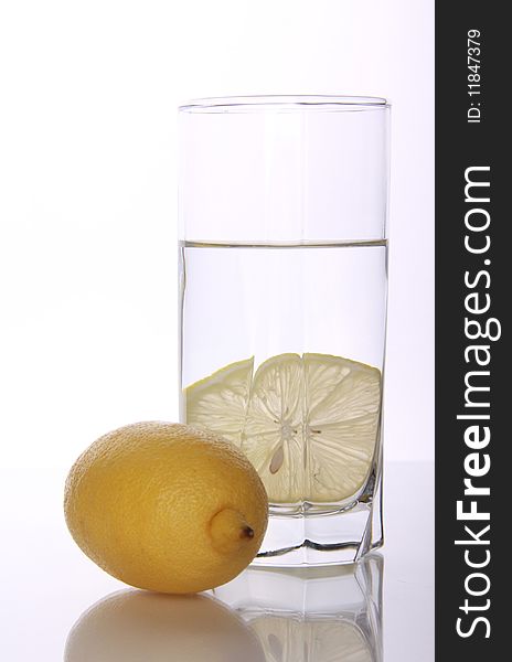 Glass with water and slice refreshing lemon on mirror table. Glass with water and slice refreshing lemon on mirror table