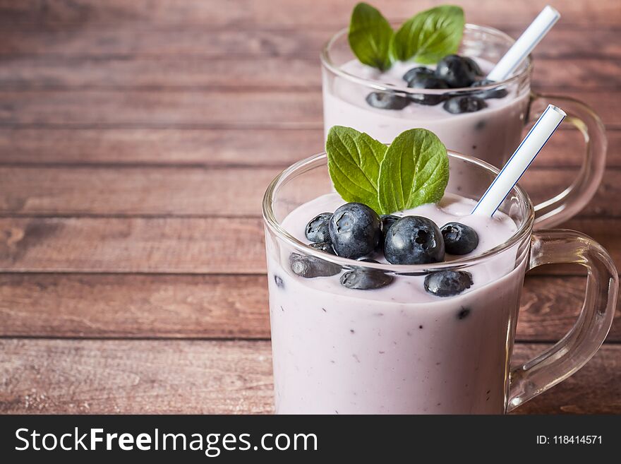 Blueberry yogurt in glass cups with fresh blueberries and mint on a wooden rustic table.