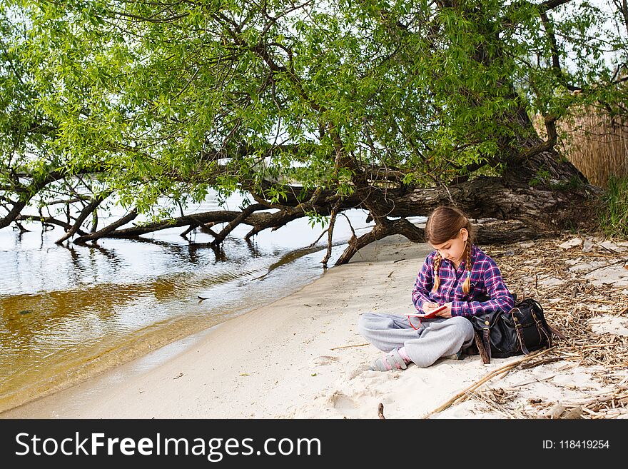 Little girl with backpack relaxing on the beach near by tree