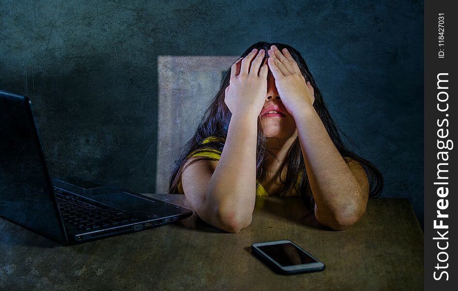 Dramatic portrait of young latin sad and scared woman covering face with hands desperate and depressed with laptop and mobile phone in cyber bullying and internet problem. Dramatic portrait of young latin sad and scared woman covering face with hands desperate and depressed with laptop and mobile phone in cyber bullying and internet problem