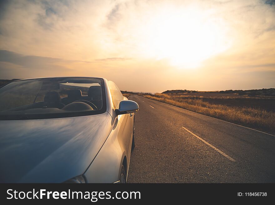 Travelling. Fashionable luxury empty car with open roof is parking on road. Wonderful sunset with sky in background. Copy space in the right e. Travelling. Fashionable luxury empty car with open roof is parking on road. Wonderful sunset with sky in background. Copy space in the right e