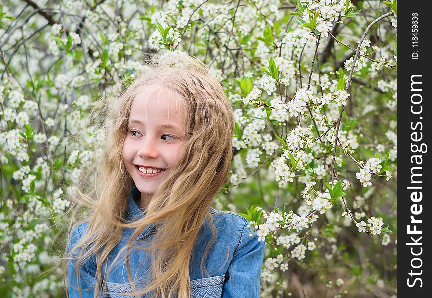 Portrait of a beautiful girl in a denim shirt next to a cherry tree. Portrait of laughing happy girl.